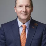 A portrait image of Nunzio Quacquarelli, Founder and President of QS, wearing a blue suit with an orange tie.